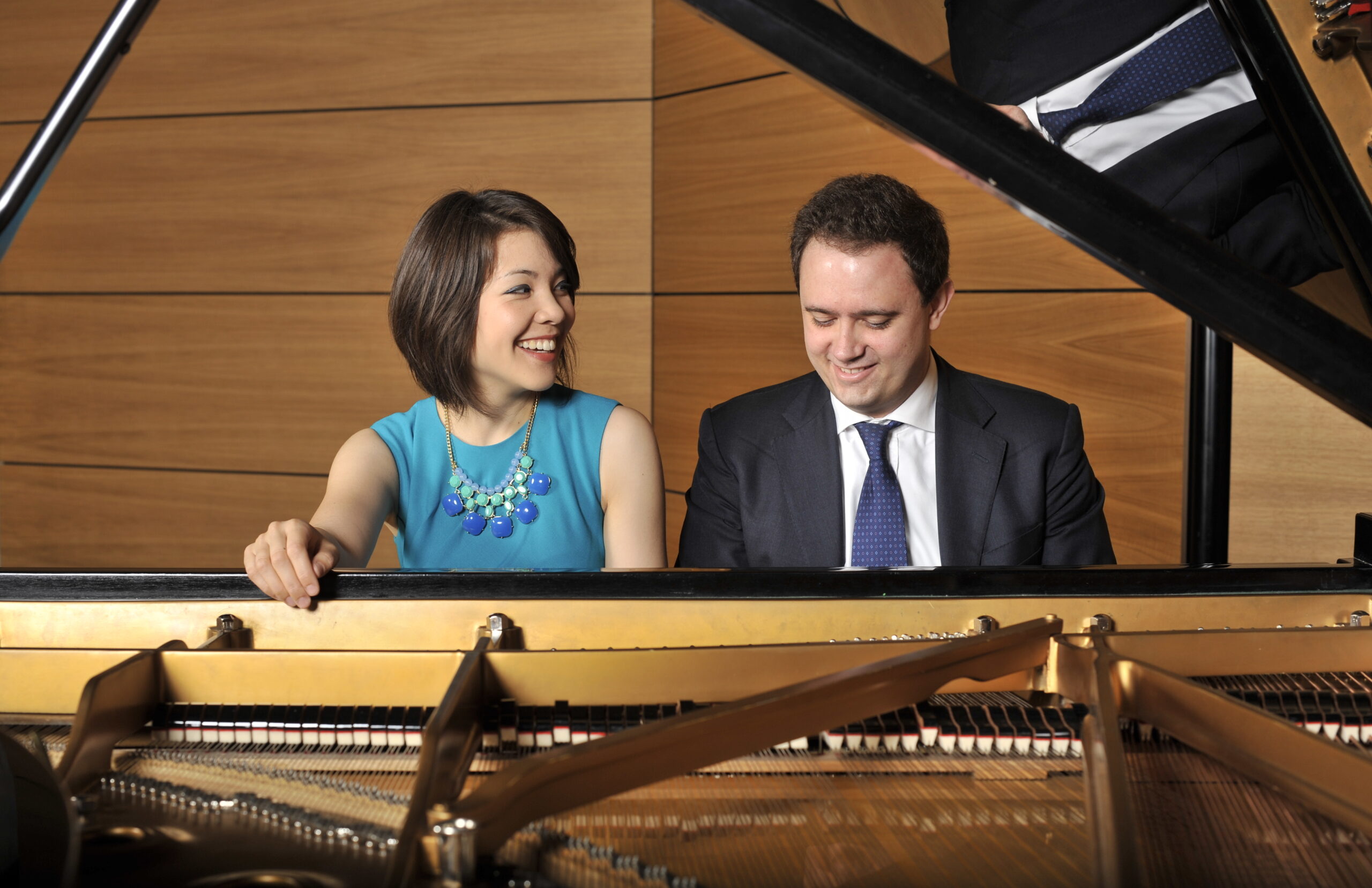 A woman and a man both sitting behind a piano