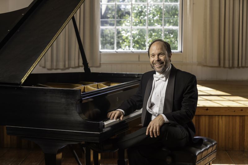 Pianist Fred Moyer sitting in front of a piano with his arms on the keys